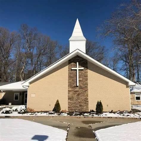 The Immanuel Baptist Church building on a clear winter morning — a white steeple above a brick gable with a tall white cross, snow still on the lawn
