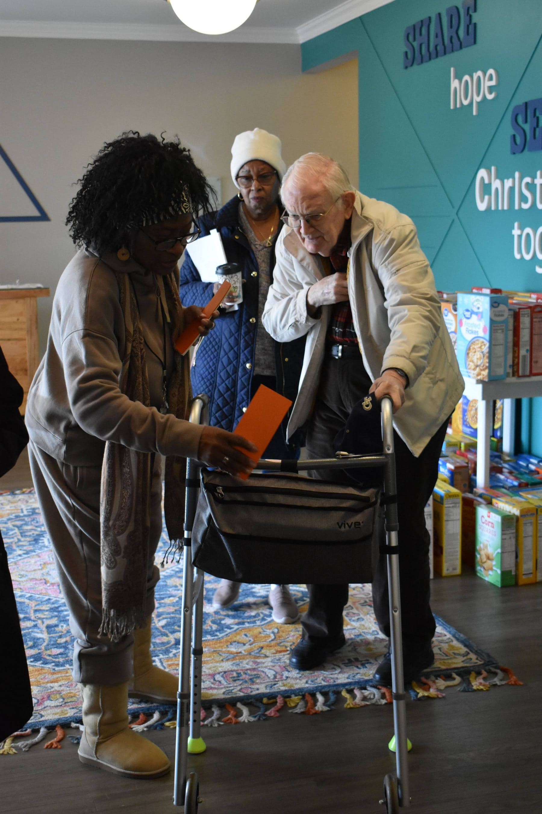 Members handing out groceries in the fellowship room, in front of the teal wall lettered Share Hope, Serve Christ Together