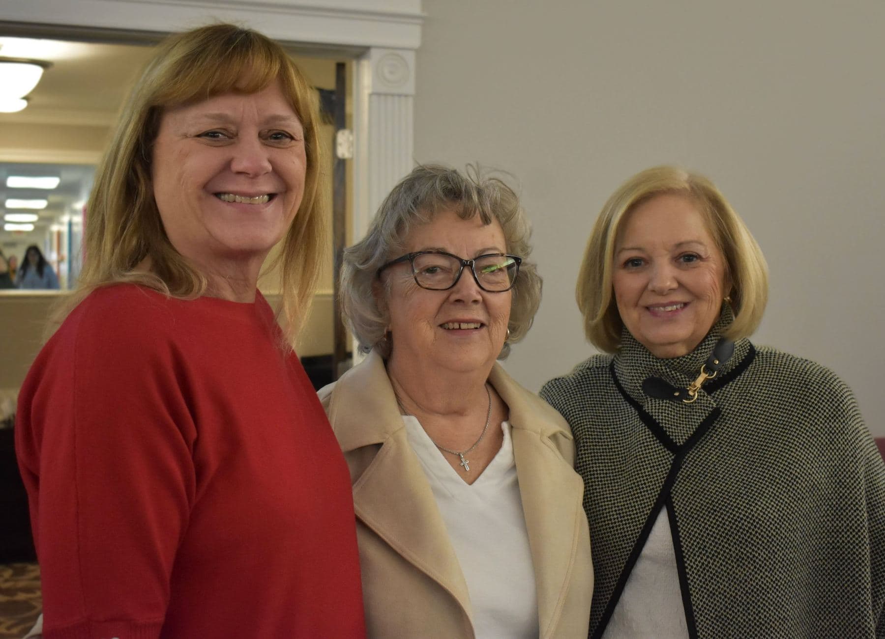 Three women of the church standing together in the hallway before the service, smiling at the camera