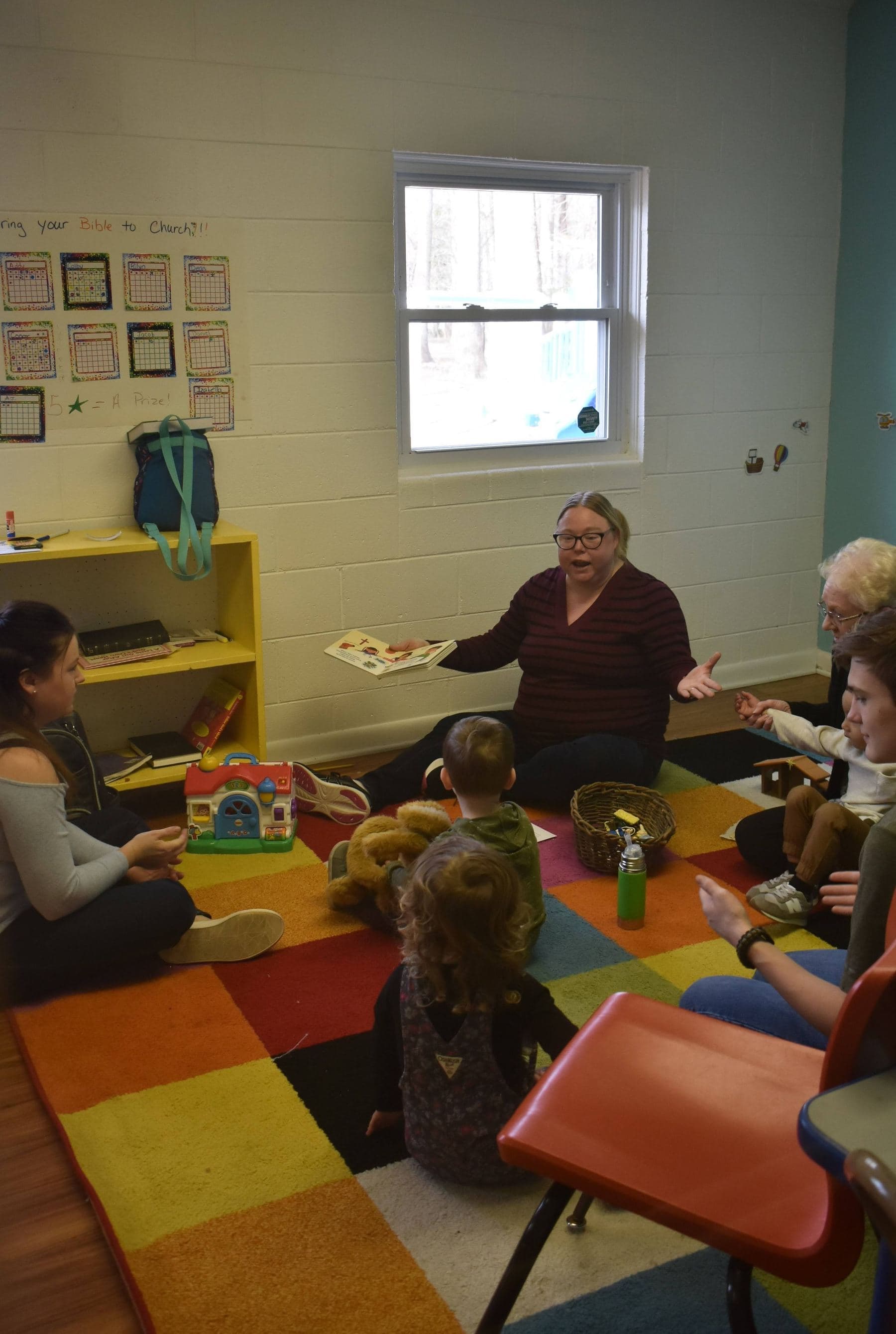 A teacher on the floor with a circle of children on a bright patchwork rug during Sunday class