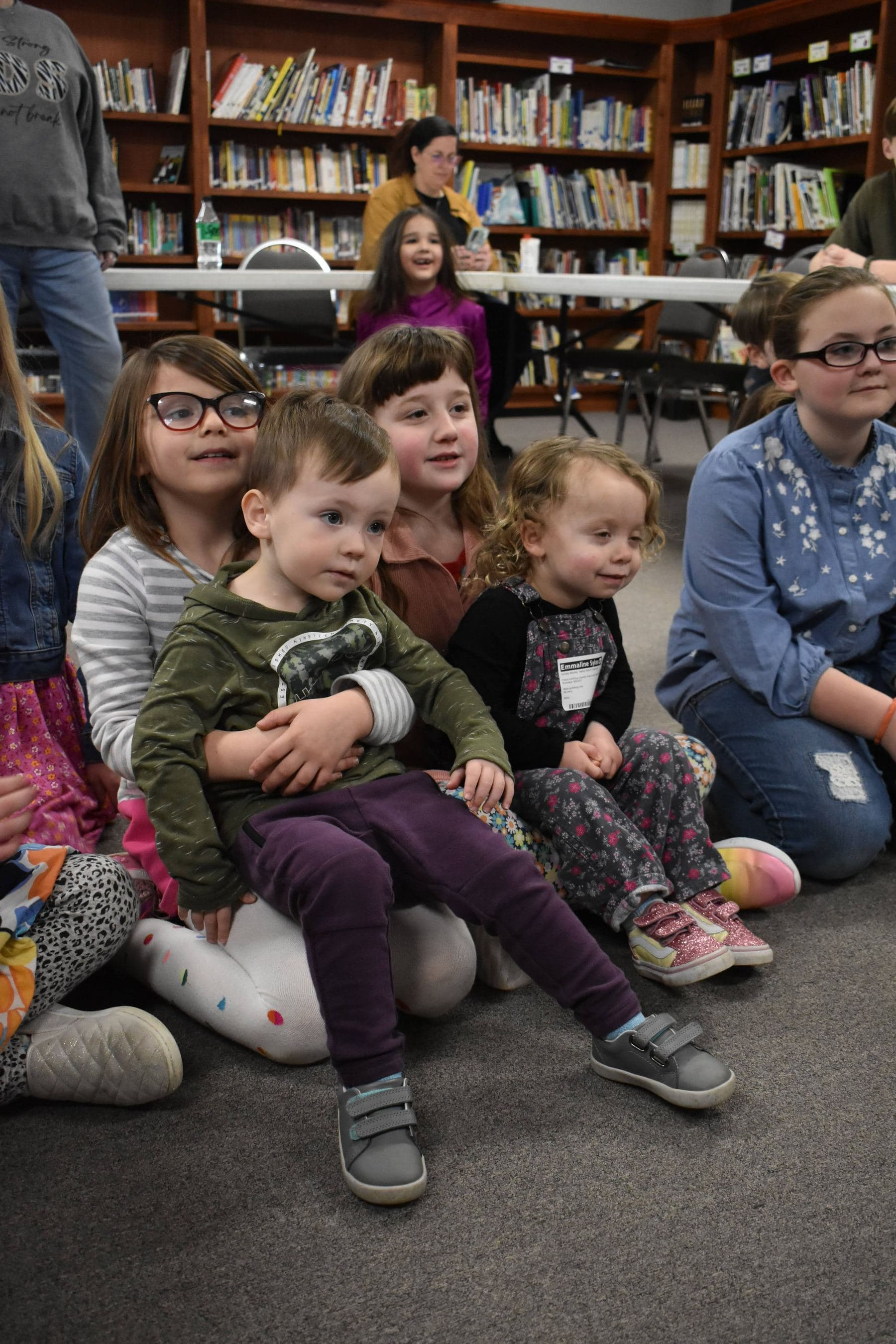 Older girls looking after the younger children on the floor of the church library, one holding a toddler on her lap