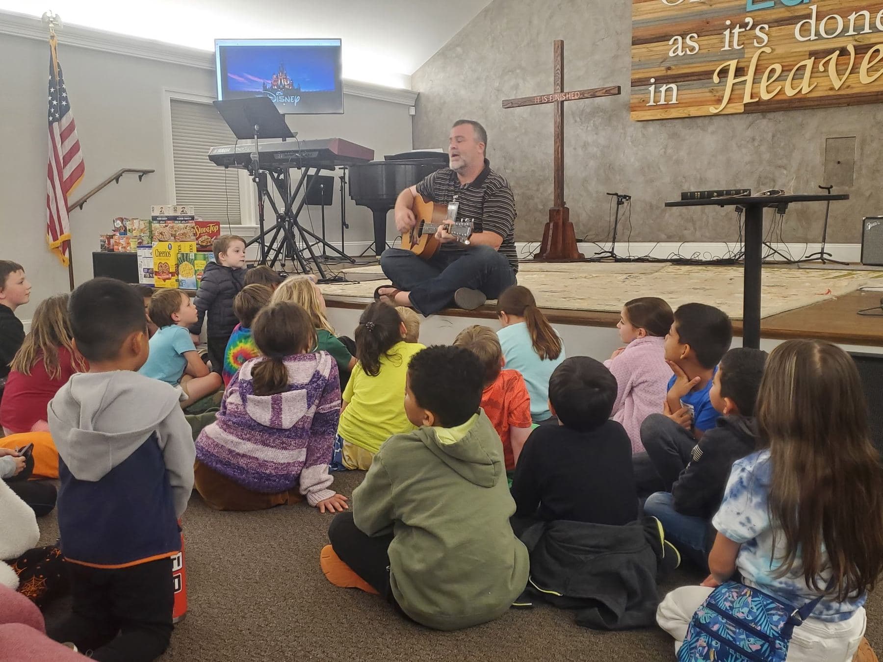 A room full of children sitting on the floor while a leader plays guitar for them at Parents' Night Out