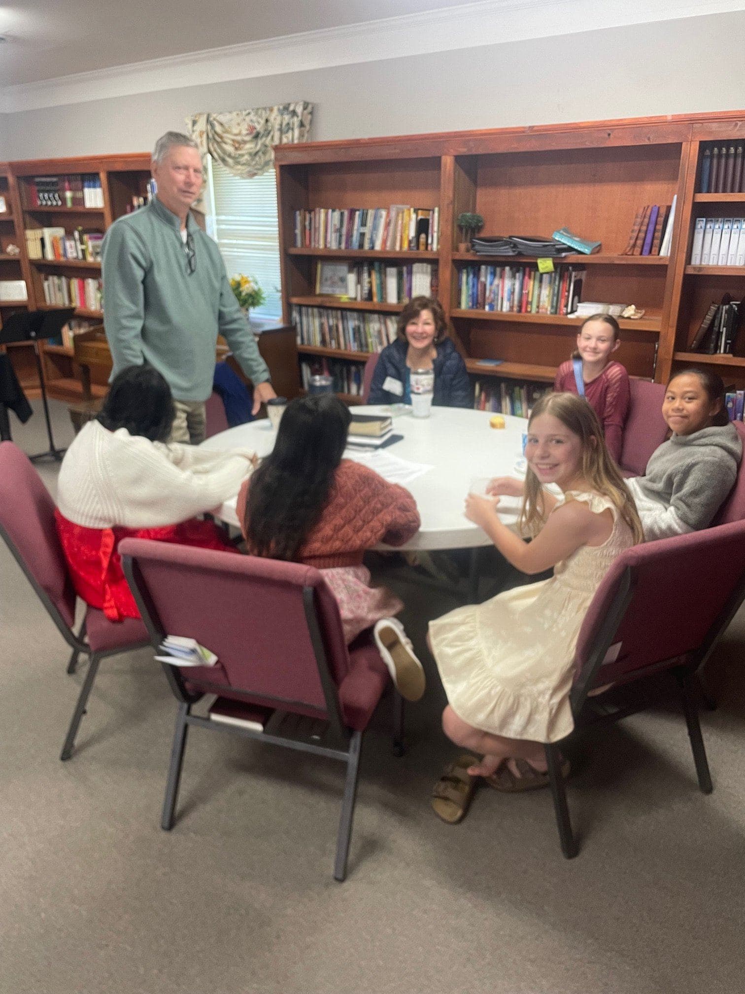 A teacher standing to lead a preteen class seated around a table in the church library