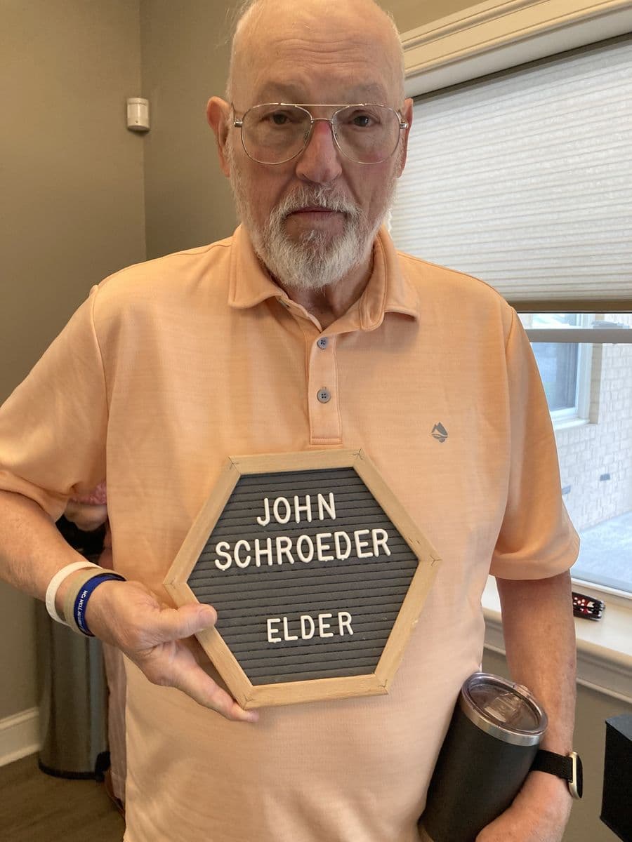 John Schroeder holding a letterboard reading John Schroeder, Elder