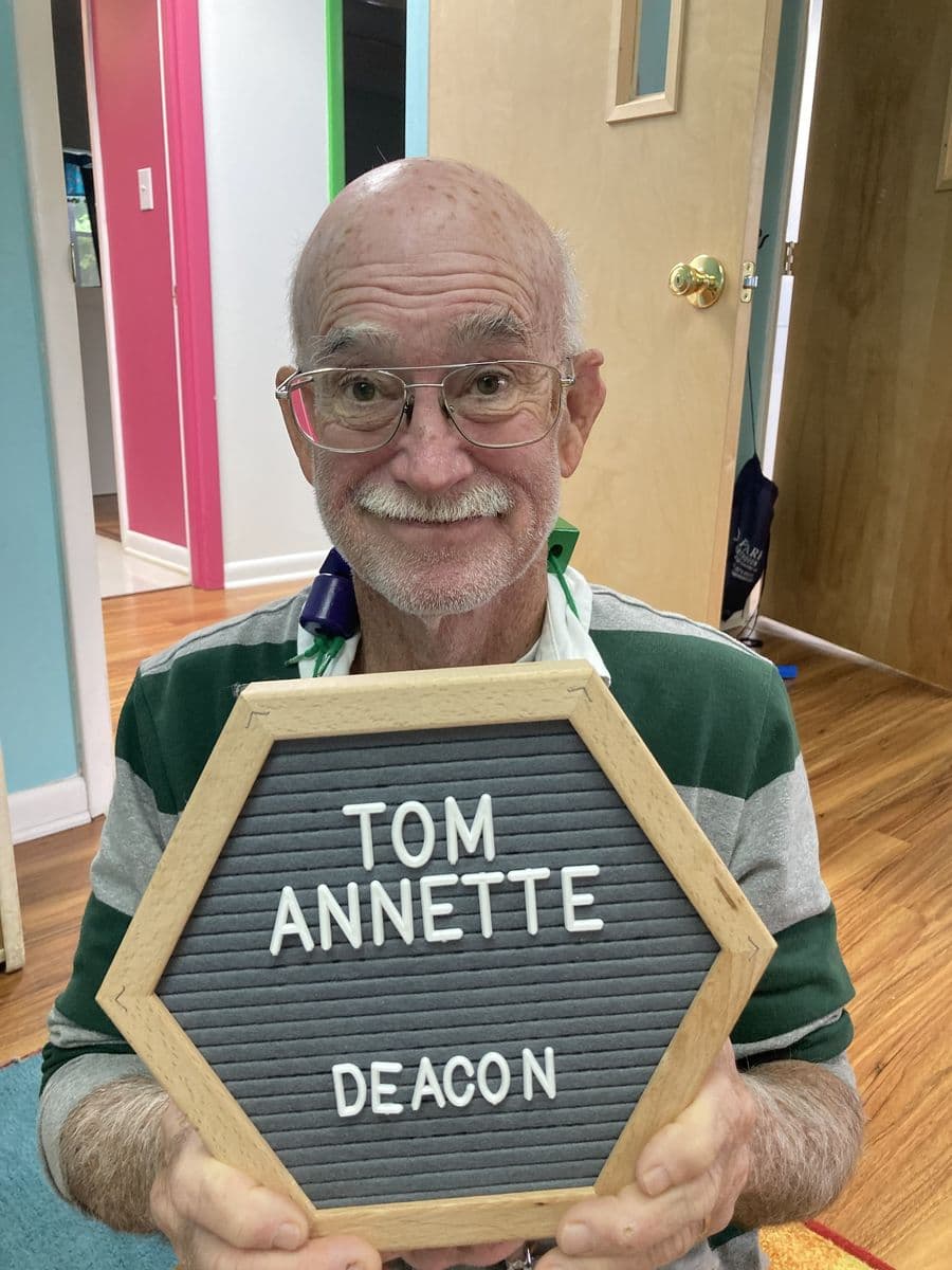 Tom Annette holding a letterboard reading Tom Annette, Deacon
