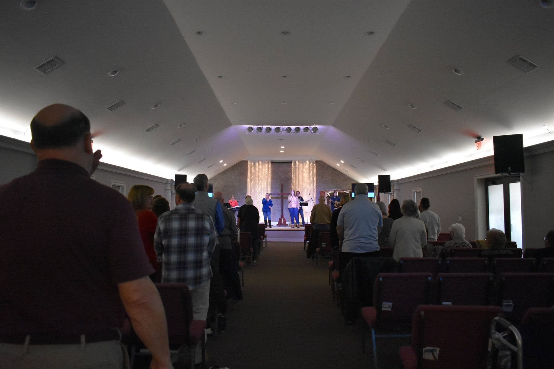 The worship team leading from the platform beneath a wooden cross, the congregation standing in the rows ahead