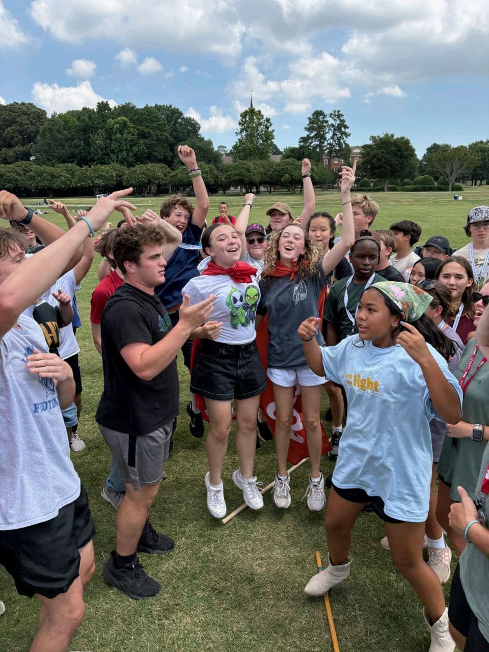 Students cheering on an open field at summer camp, arms raised